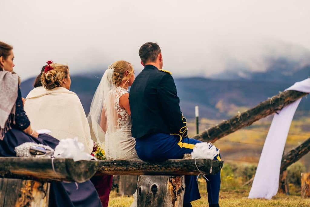 A La Crosse WI wedding photographer captures a bride and groom sitting on a bench in the mountains.
