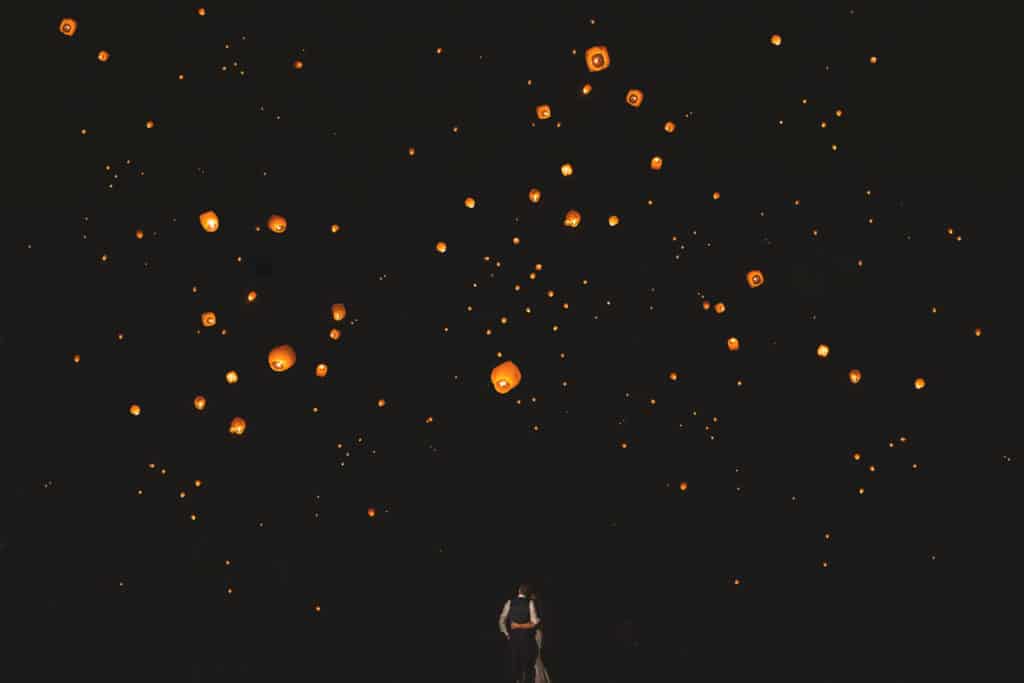 A man standing in the middle of a field with lanterns in the sky.
