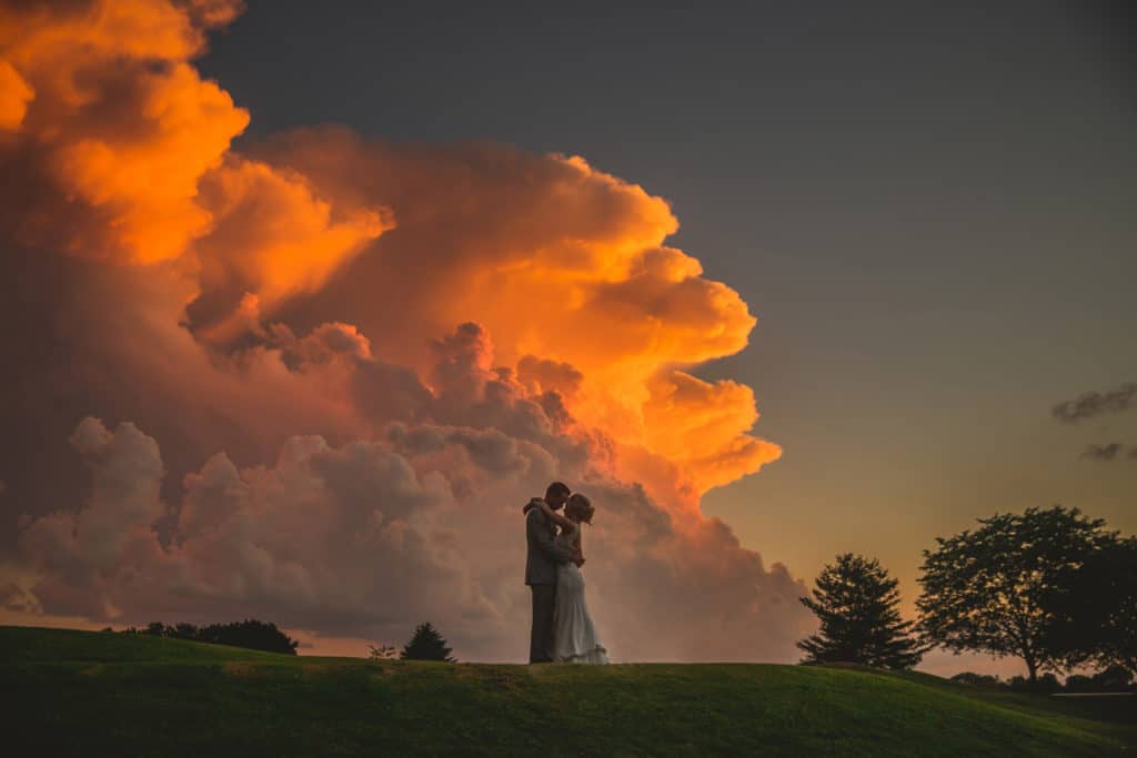 A bride and groom kiss in front of a cloud during a crazy storm wedding.
