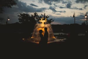 A couple standing in front of a fountain at dusk.