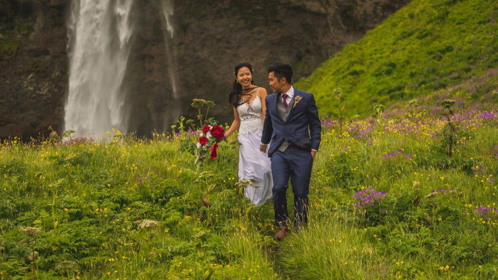 A bride and groom standing in front of a waterfall.