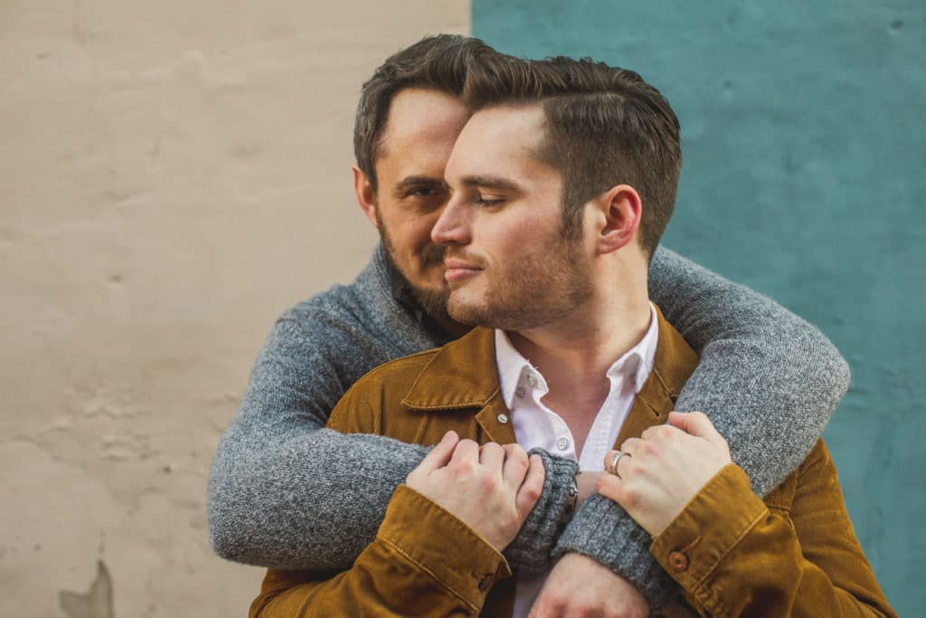 Two men hugging in front of a wall.