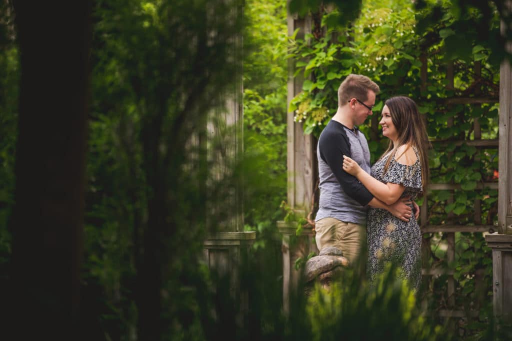 A couple embraces under a gazebo in a garden.