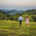A couple walking through a grassy field at sunset.