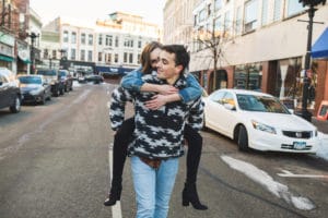 A man is carrying a woman in the middle of a city street.