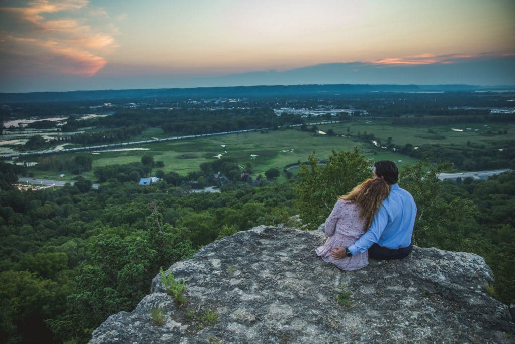 A couple sitting on top of a rock overlooking a valley.