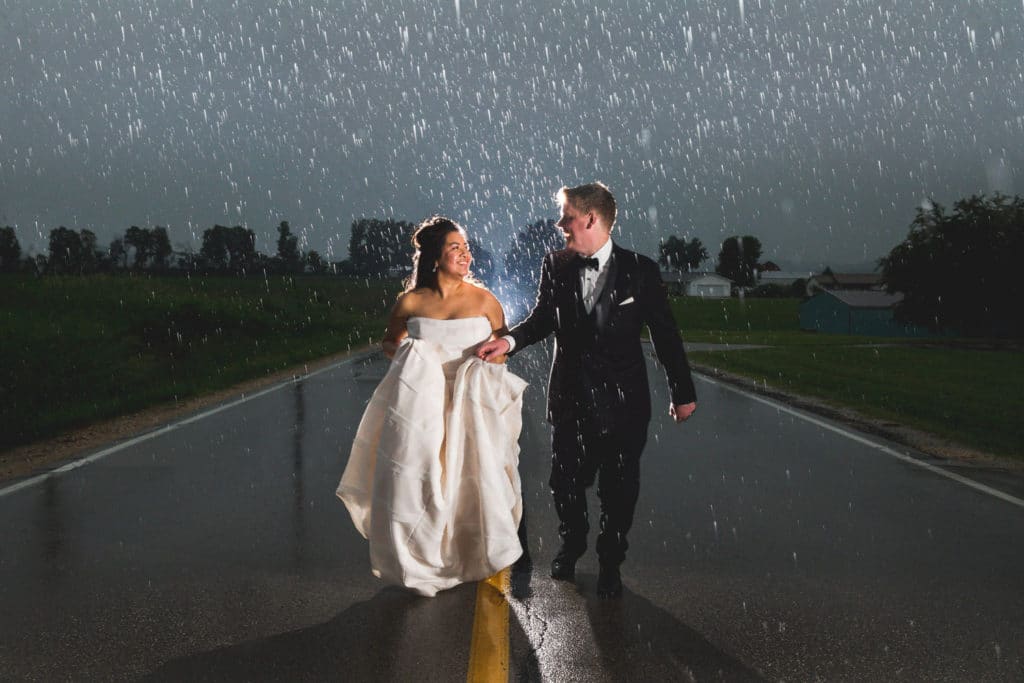A bride and groom standing in the rain on a road.