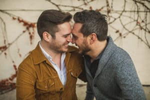 Two men are smiling at each other in front of a wall.