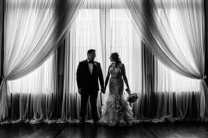 A wedding ceremony at 4 Sisters Wine Bar with the bride and groom standing in front of curtains.