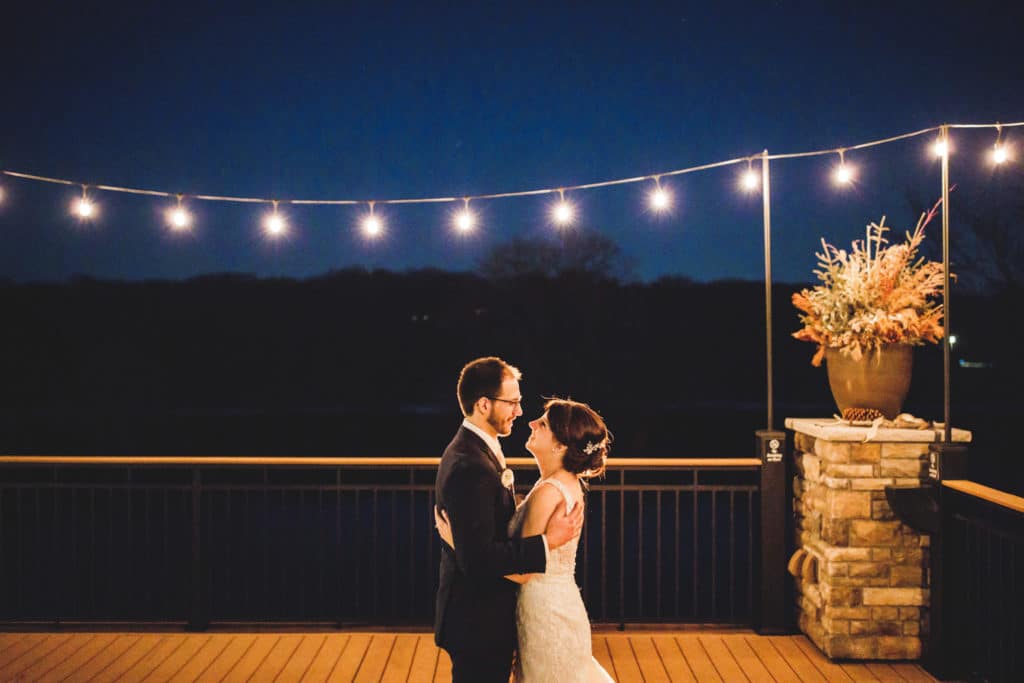 A bride and groom standing on a deck at Leopolds Mississippi Gardens at night with string lights.