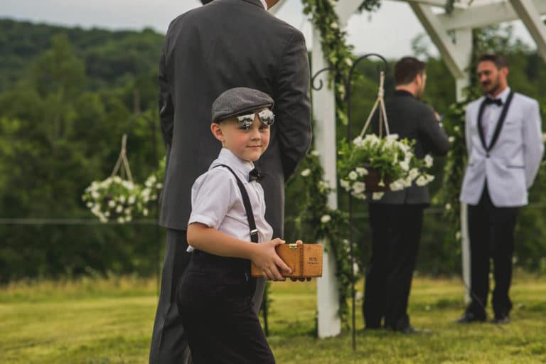 A young boy wearing a hat and glasses at a wedding.