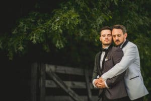 Two grooms hugging in front of a fence.
