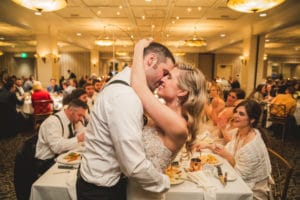 A couple, joined by their beloved dog, sharing a kiss at their wedding reception.