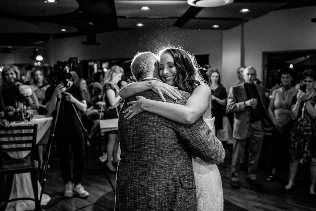 A black and white photo of a bride hugging her father at a wedding reception at 4 Sisters Tapas.