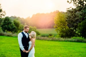 A bride and groom standing in a field at sunset.