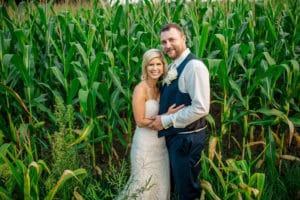 A bride and groom standing in a corn field during an On A Whim Barn Wedding.