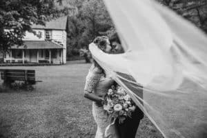 A Norskedalen wedding couple sharing a kiss under a veil in front of a house.