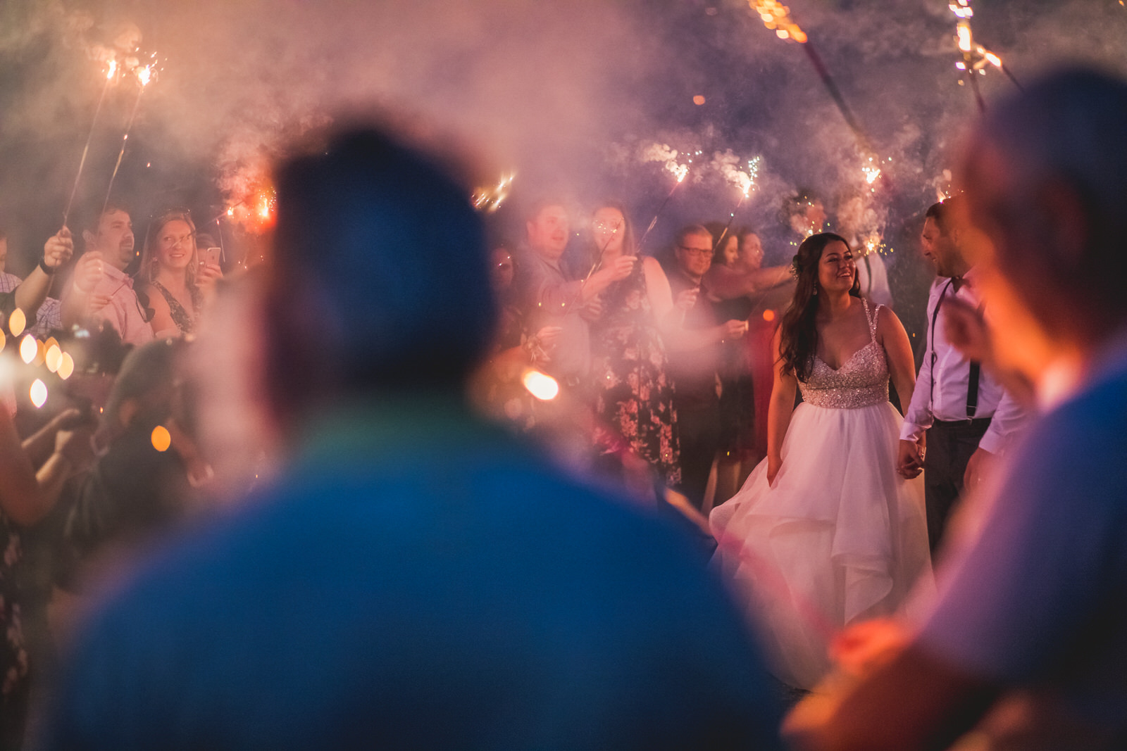 A bride and groom walking down the aisle with sparklers.