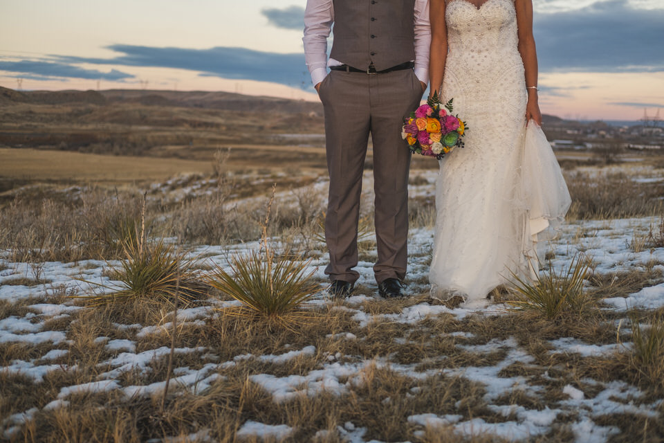 A bride and groom standing in a field with snow on the ground.