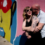 A man and woman hugging in front of a colorful wall.