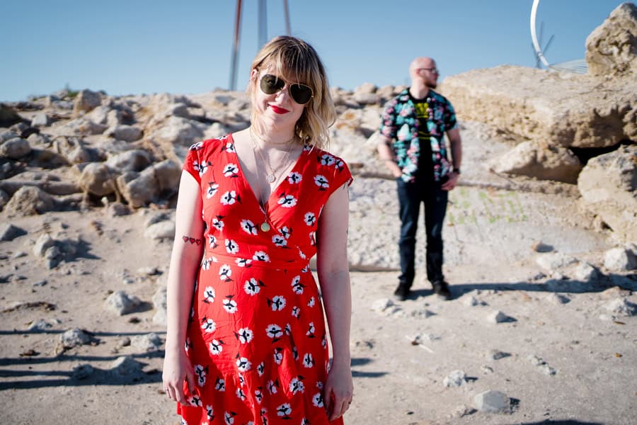 A woman in a red dress standing in front of a rock.