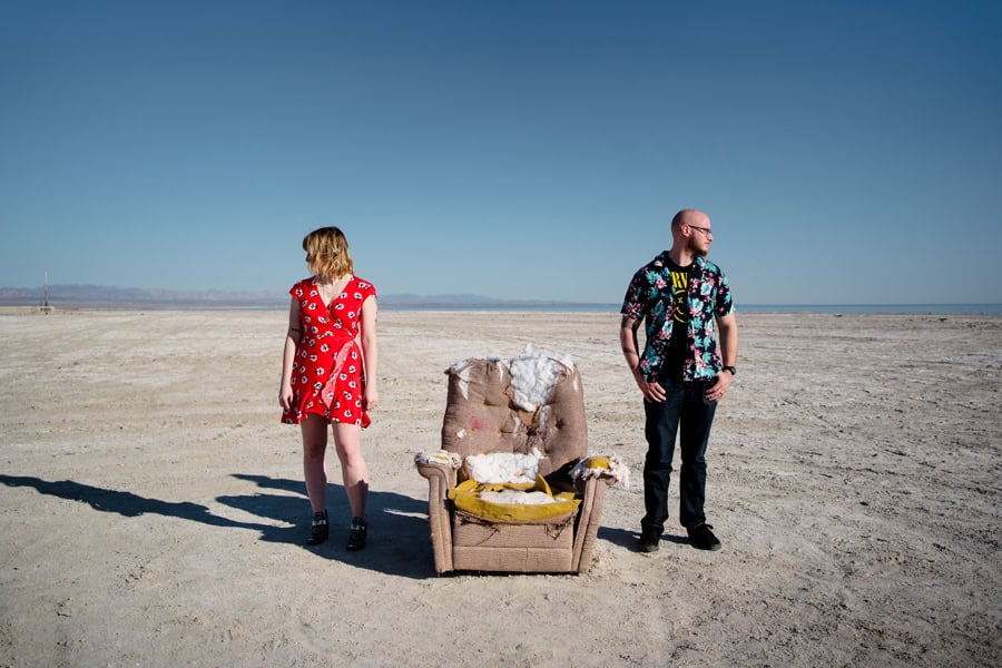 A man and woman standing next to a chair in the desert.
