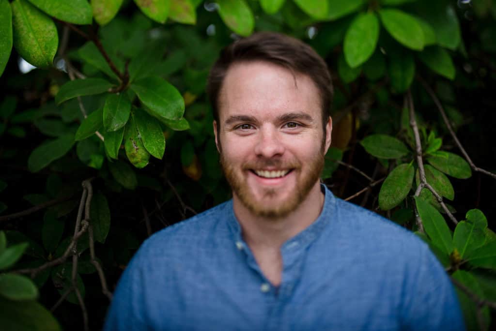 A man smiling in front of green leaves.