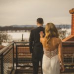 A bride and groom standing on a balcony overlooking a snowy landscape.