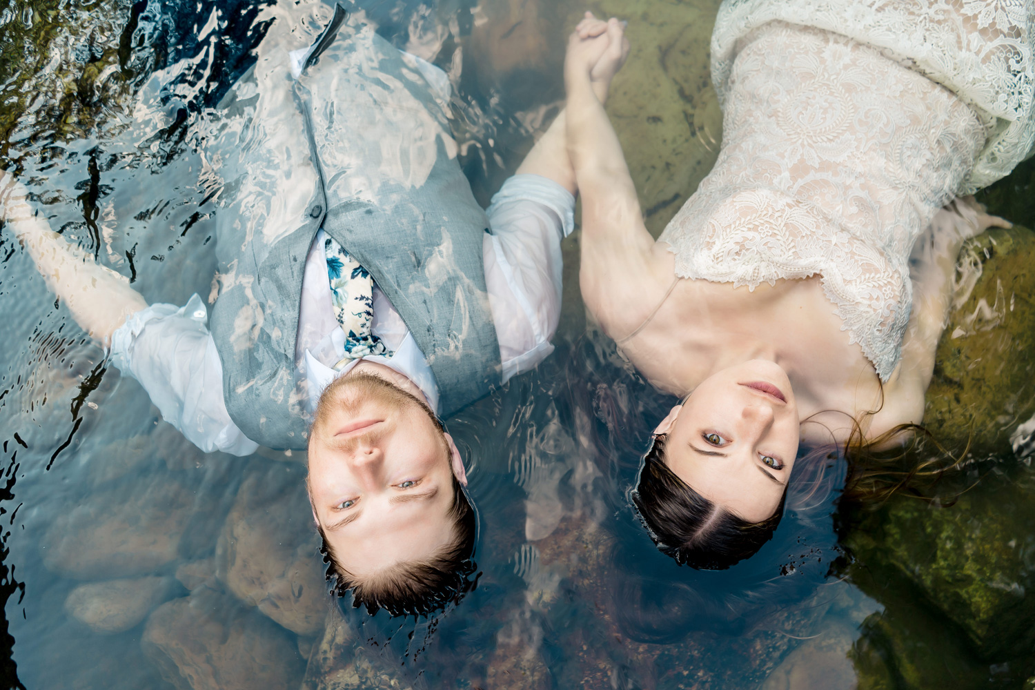 A bride and groom laying in the water.