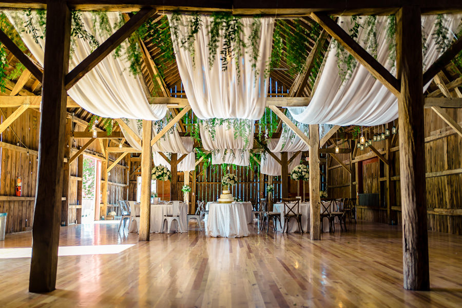 A wedding reception in a barn with greenery hanging from the ceiling.