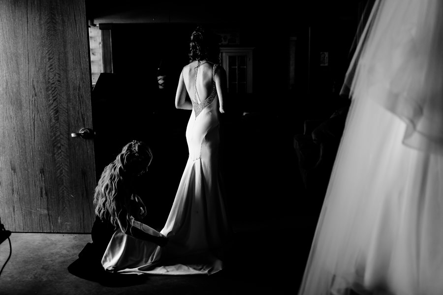 A bride is putting on her wedding dress in a dark room.
