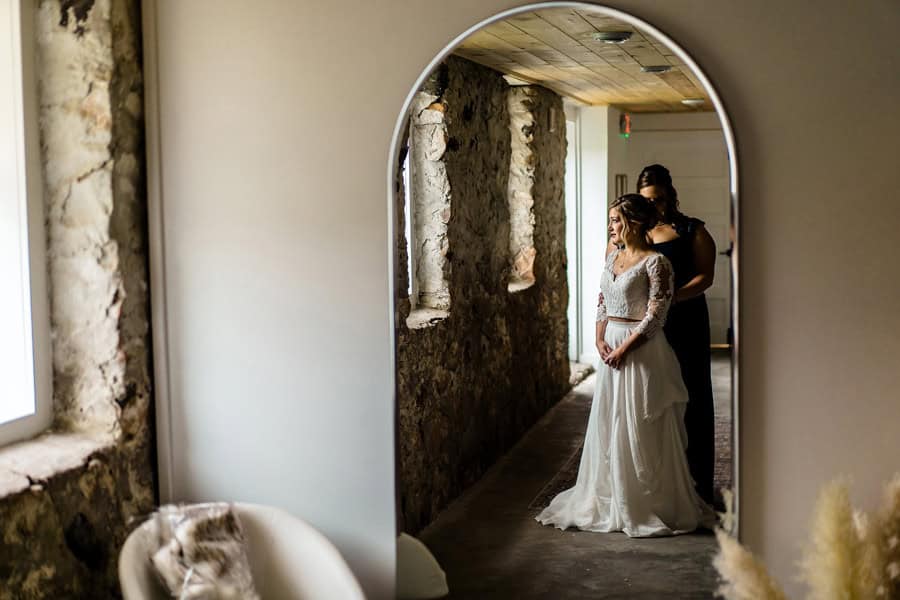 A bride and her bridesmaid standing in front of a mirror.