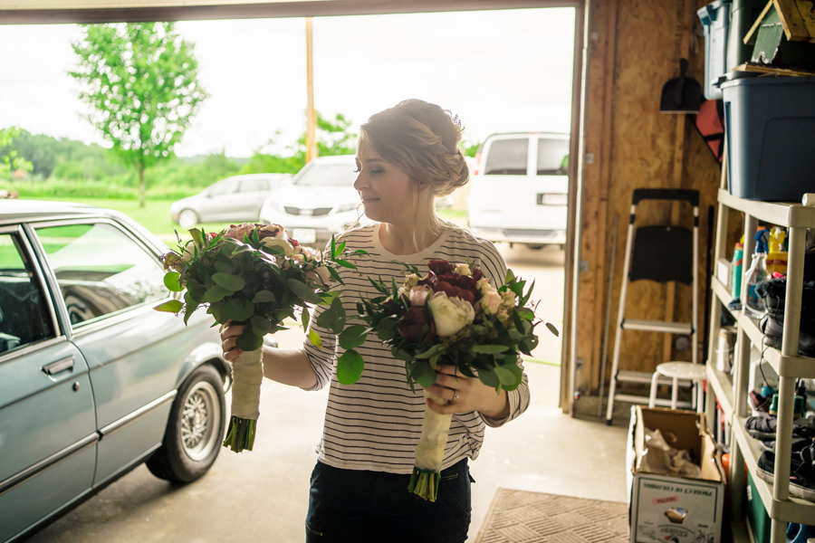 A woman holding bouquets in front of a car in a garage.