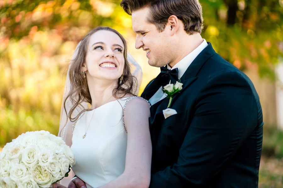 A bride and groom are smiling in front of a tree.