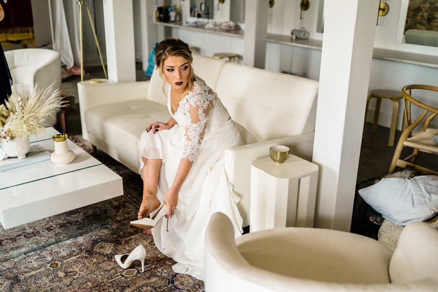 A bride putting on her wedding shoes in a living room.