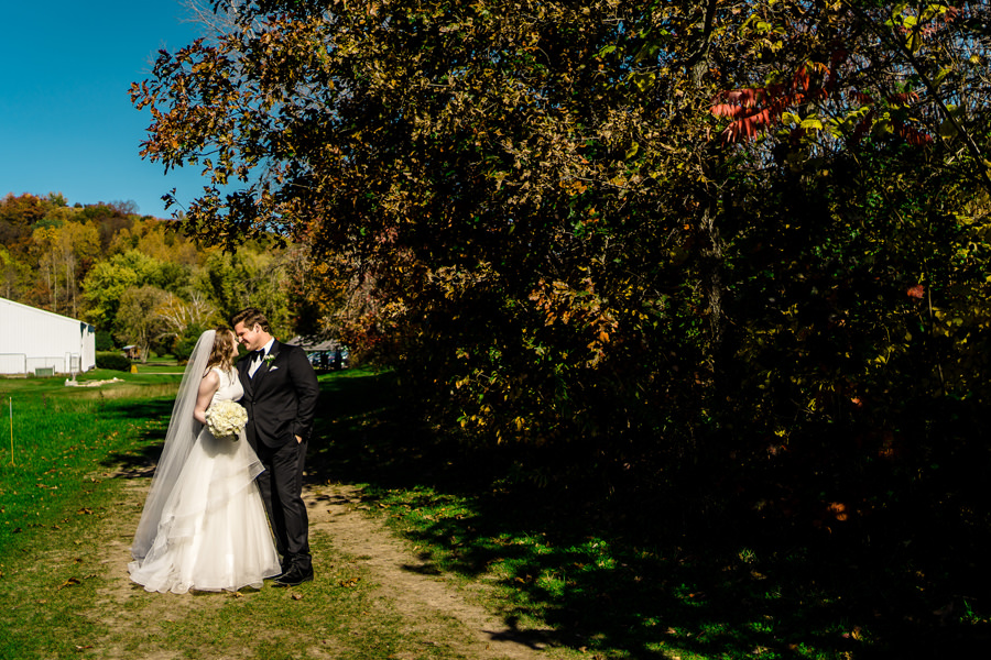 A bride and groom kissing on a path in the fall.