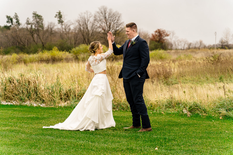 A bride and groom high fiving in a field.