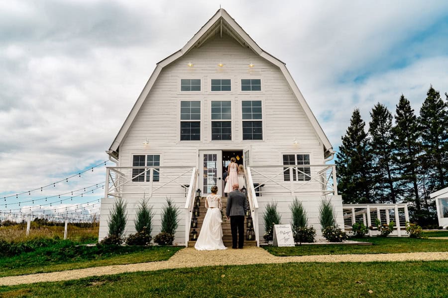 A bride and groom standing outside of a white barn.