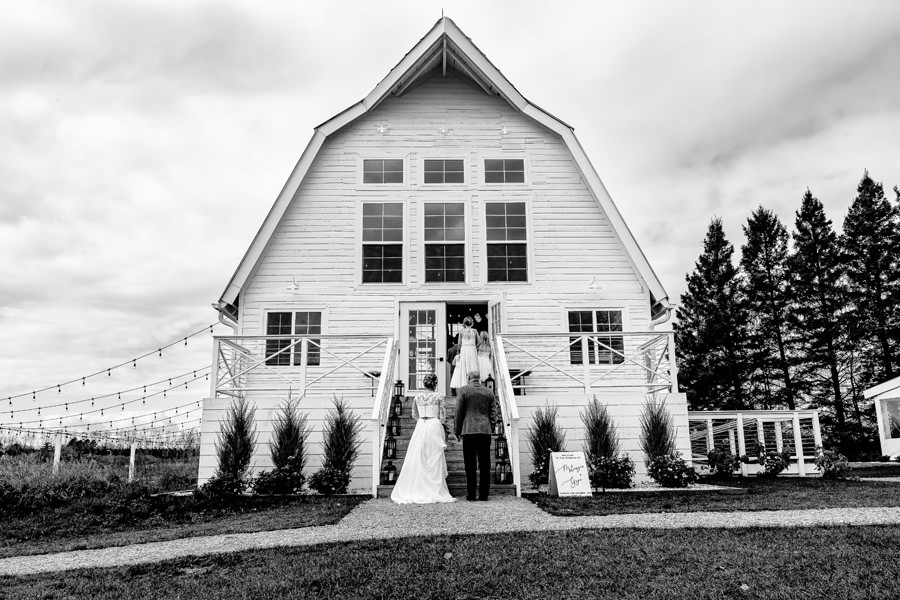 A black and white photo of a bride and groom standing outside of a barn.