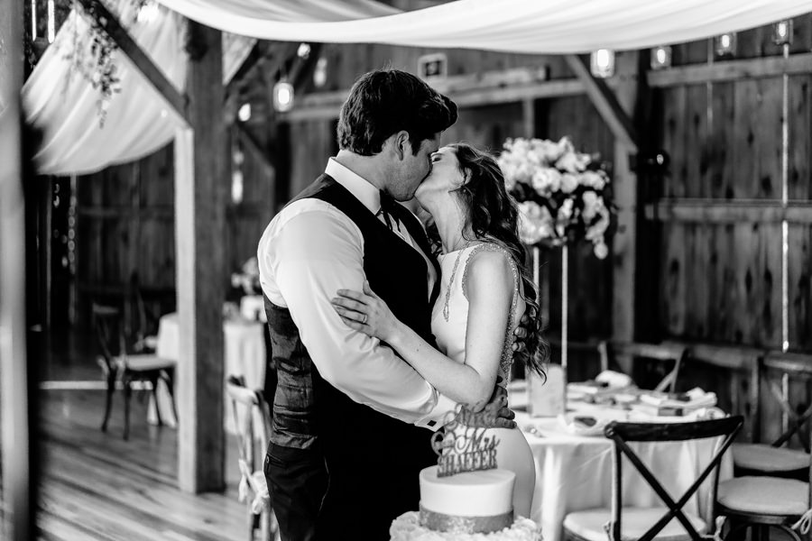 A bride and groom kiss in front of their wedding cake.