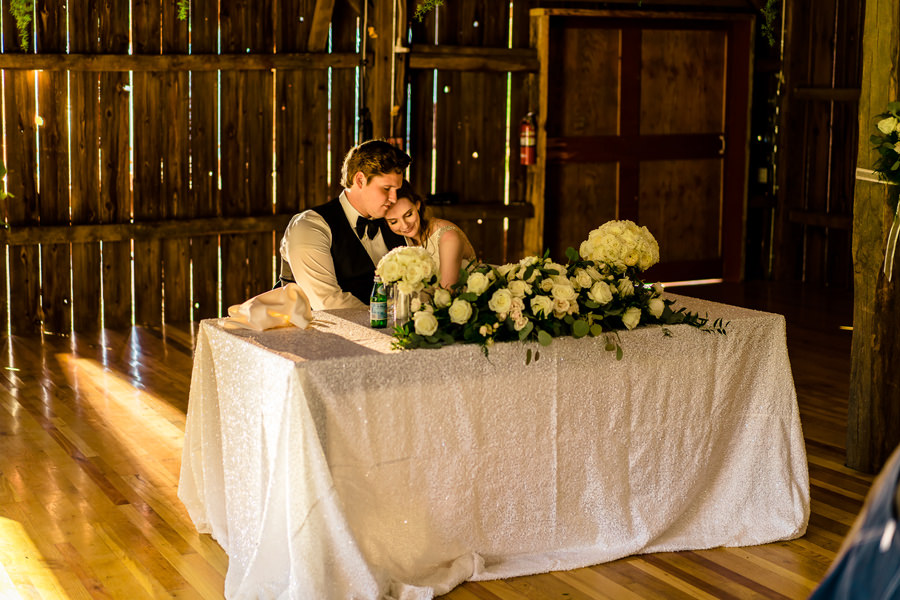 A bride and groom sitting at a table in a barn.