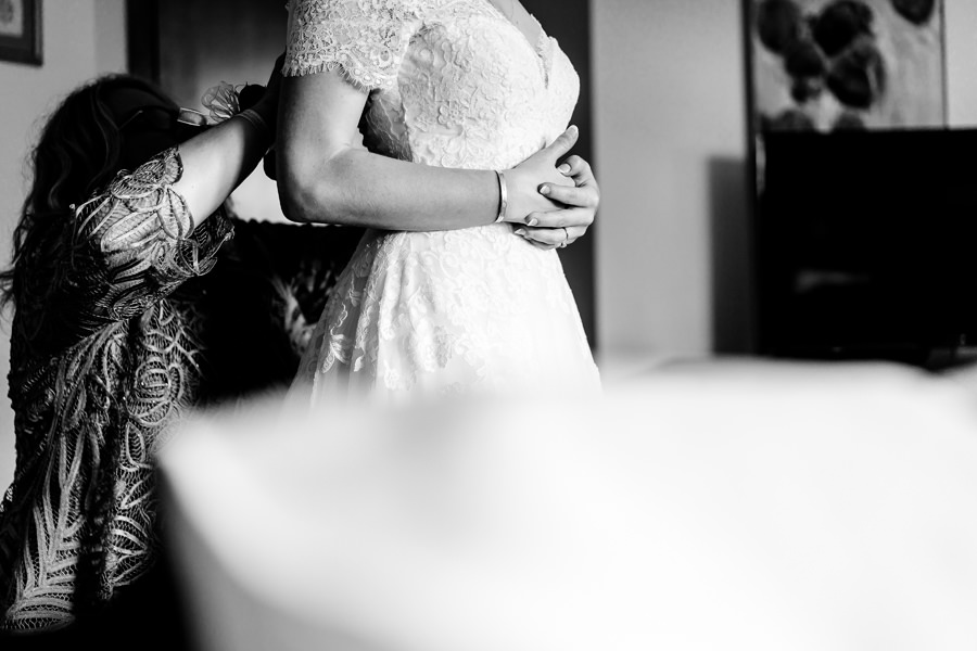 A bride putting on her wedding dress in a black and white photo.
