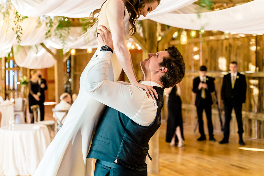 A bride is being lifted up by her groom in a barn.