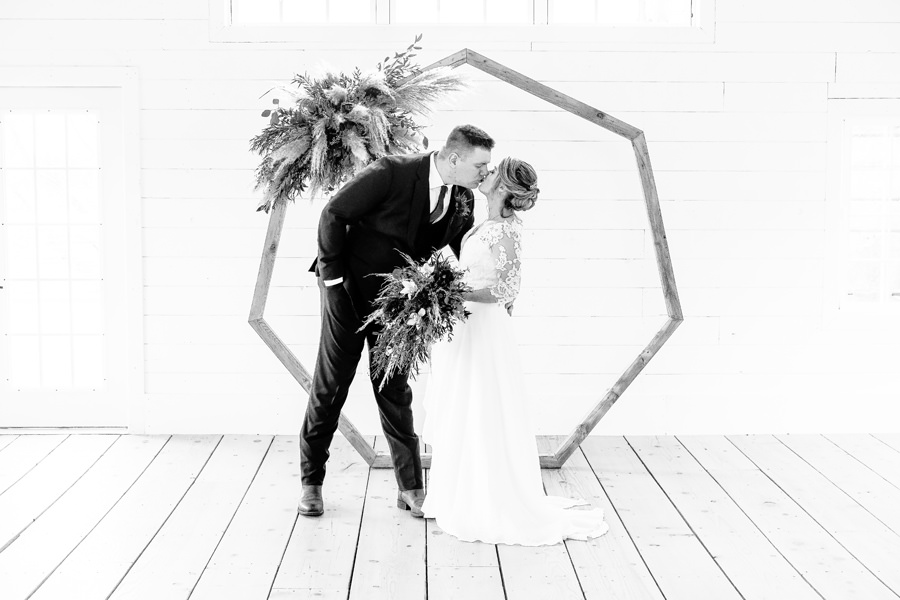 A bride and groom kissing in front of a hexagonal wedding arch.