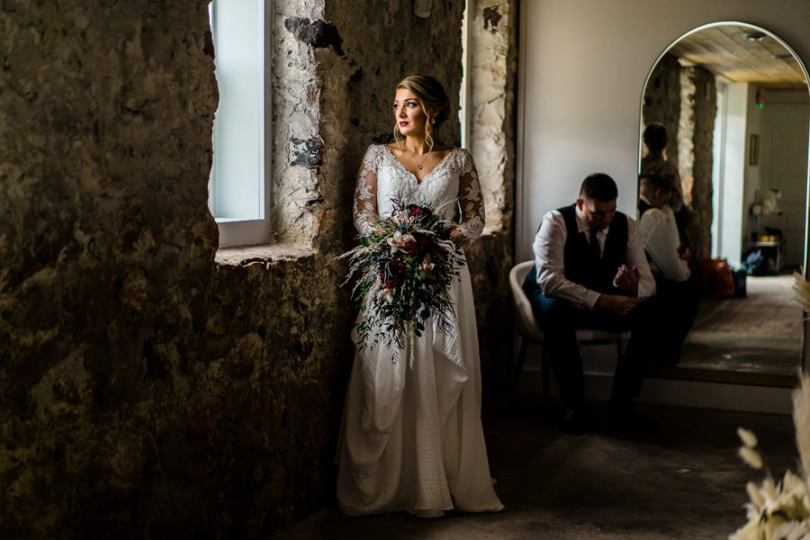 A bride standing in front of a mirror in a stone room.