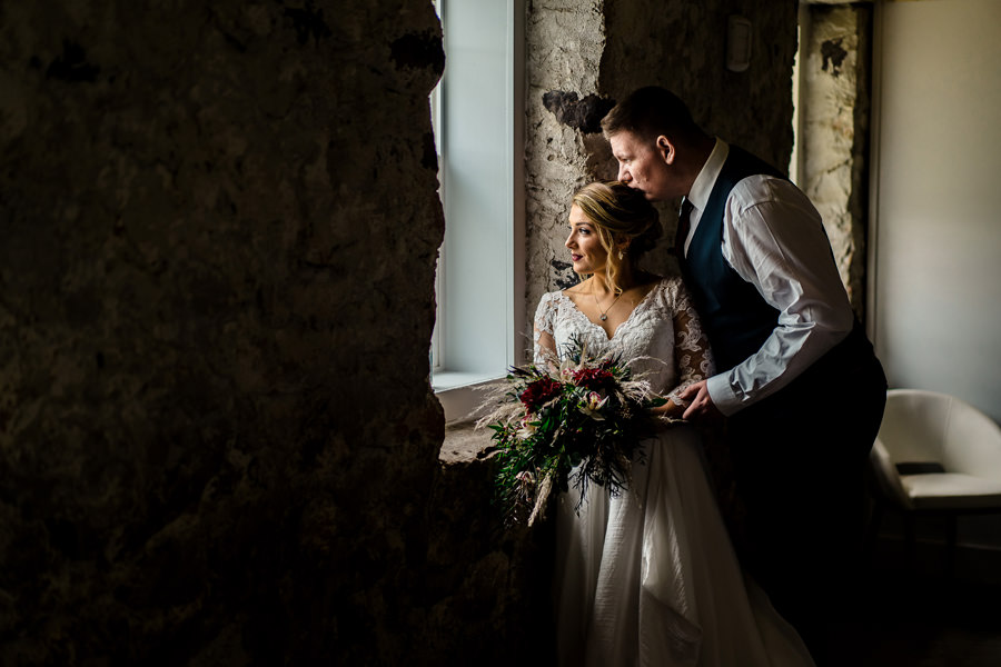 A bride and groom standing by a window in an old building.