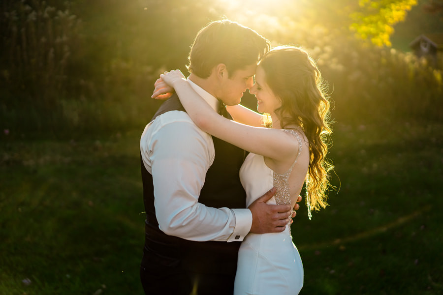 A bride and groom embrace at sunset in a field.