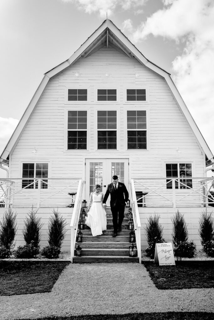 A bride and groom walking down the steps of a white barn.