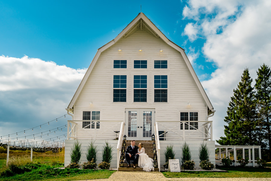 A bride and groom standing in front of a white barn.