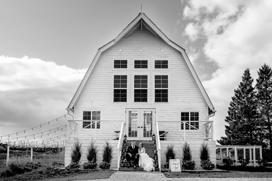 A bride and groom standing in front of a white barn.